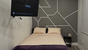 A modern bedroom with a bed, a mounted TV, and geometric wall design.