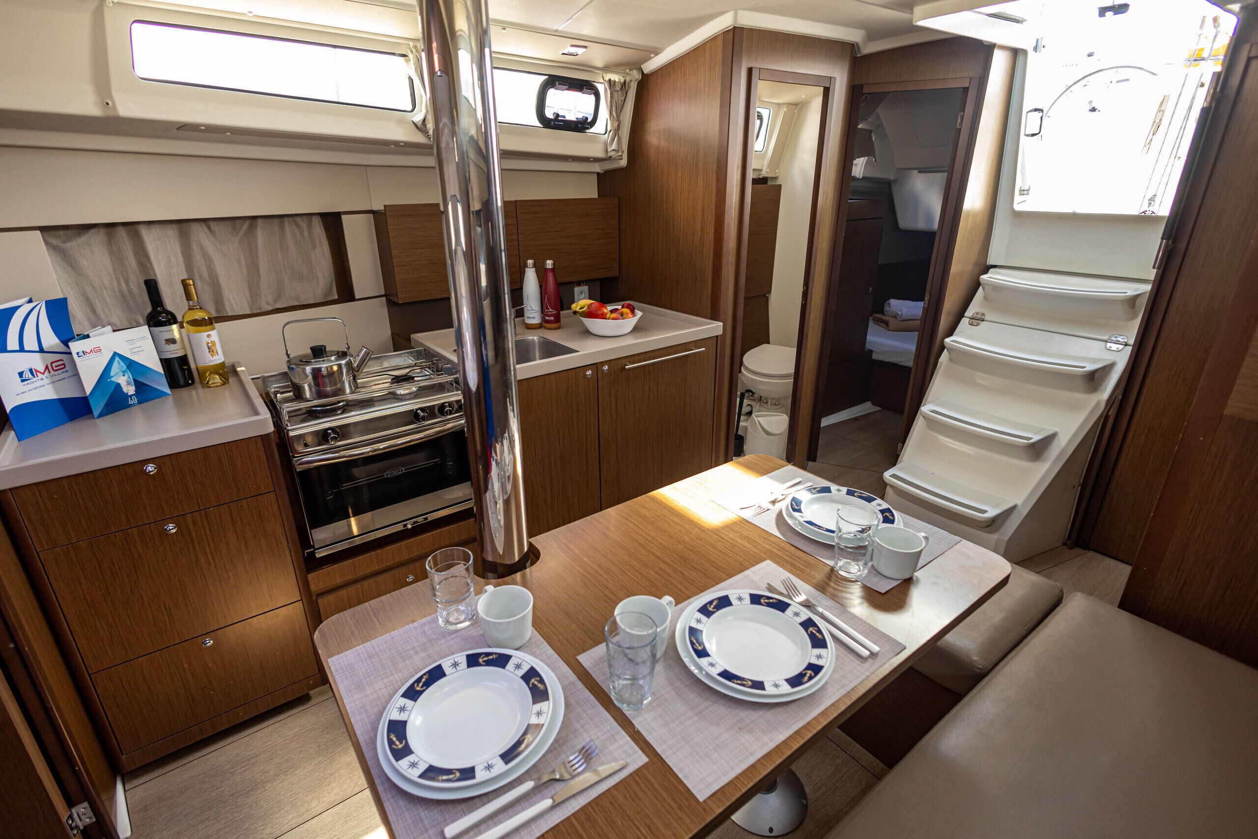 A compact kitchen with a stove, sink, and a dining area set for two with plates, cutlery, and a bowl of fruit.