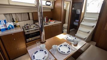 A compact kitchen with a stove, sink, and a dining area set for two with plates, cutlery, and a bowl of fruit.