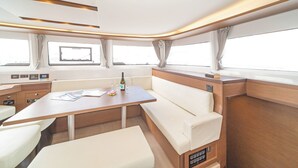 Interieur van een jacht met een eethoek, comfortabele zittingen, bedieningspanelen en grote ramen.