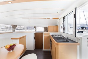 A compact galley with a sink, stove, and storage cabinets, large windows offering views of the marina. - Sun-Kissed Sailing Adventure in Islas Sarónicas (Alimos)