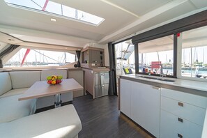 A yacht's interior with a dining area, kitchen, and a view of the marina.