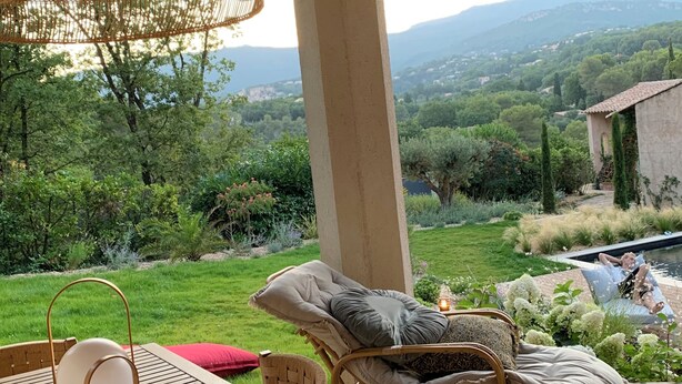 Un espacio al aire libre techado con mobiliario de mimbre, una mesa y vistas a un paisaje exuberante.