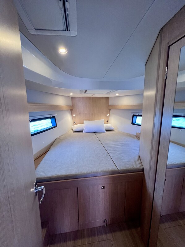 A compact, well-lit cabin with a bed, two monitors, and a wooden headboard.