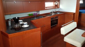 A compact kitchen with wooden cabinets, a sink, a stove, and a small seating area. - Sun-Kissed Sailing Adventure in the Ionian Islands, Lefkada (Lefkada)