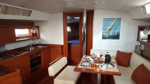 A compact galley with a stove, oven, and sink; a dining area with a table set for two; and a cozy seating area with cushions. - Sun-Kissed Sailing Adventure in the Ionian Islands, Lefkada (Lefkada)