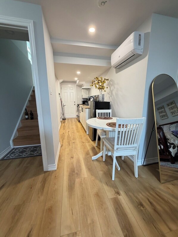 A modern kitchen with white cabinetry, a dining table with chairs, and an air conditioning unit mounted on the wall.