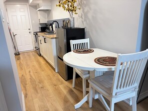 A compact kitchen with a white table and chairs, a refrigerator, and a vase with yellow flowers.