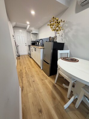 A compact kitchen with a dining table, a refrigerator, and a vase with flowers.