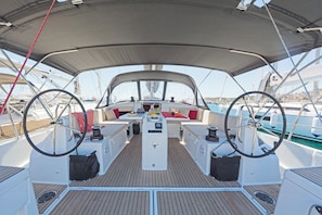 Ein Bootsdeck mit einem zentralen Tisch, zwei Steuerhörnern und einem darüberliegenden Sonnensegel.