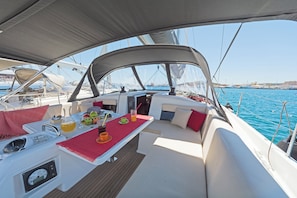 Das Deck eines Bootes mit Tisch, Sitzgelegenheiten und Blick auf den Hafen.