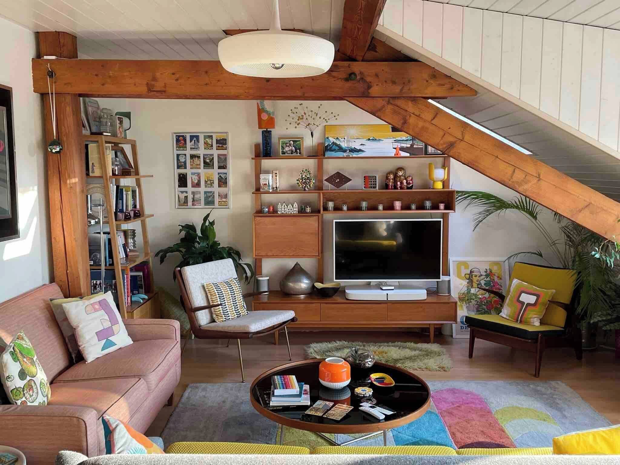 Un salon chaleureux et accueillant, avec un canapé, un fauteuil, une table basse, un téléviseur, une bibliothèque et un plafond avec des poutres apparentes.