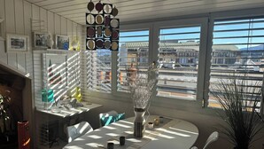 A dining area with a round table, chairs, a vase, and a view of buildings through large windows. - Stylish Loft - Amazing Views (Geneva)