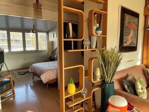 A room with a bed, a wooden shelf with decorative items, a painting on the wall, and a window with blinds. - Stylish Loft - Amazing Views (Geneva)