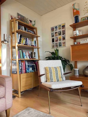 A living room with a wooden bookshelf, a patterned armchair, a potted plant, and a wall with framed pictures. - Stylish Loft - Amazing Views (Geneva)