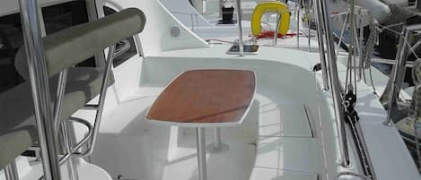 Un ponte di nave con un tavolo, ringhiere metalliche e una boa gialla.