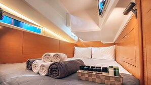 A neatly made bed with rolled towels, a bedside table with toiletries, and a headboard. - Sun-Kissed Sailing Adventure in Islas Sarónicas (Alimos)