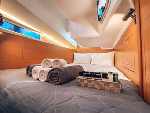 A neatly made bed with rolled towels, a bedside table with toiletries, and a headboard. - Sun-Kissed Sailing Adventure in Islas Sarónicas (Alimos)