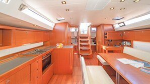 A compact kitchen with a stove, sink, and wooden cabinets. There is a small seating area with a table and a bench. - Sun-Kissed Sailing Adventure in Islas Sarónicas (Alimos)