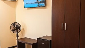 Una habitación con un armario de madera, un refrigerador negro pequeño y un ventilador de pie.