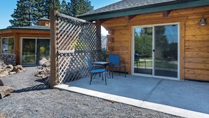 Una cabaña de madera con un patio, dos sillas y un ventanal corredero.