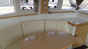 Interno di una barca con un tavolo rotondo, sedute imbottite e finestre.
