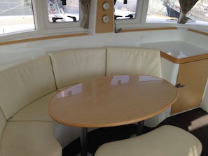 A boat interior with a round table, cushioned seating, and windows. - Sun-Kissed Sailing Adventure in Islas Sarónicas (Alimos)