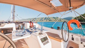 A boat deck with a steering wheel, control panel, and dining table with plates and glasses. - Sun-Kissed Sailing Adventure in Islas Sarónicas (Alimos)