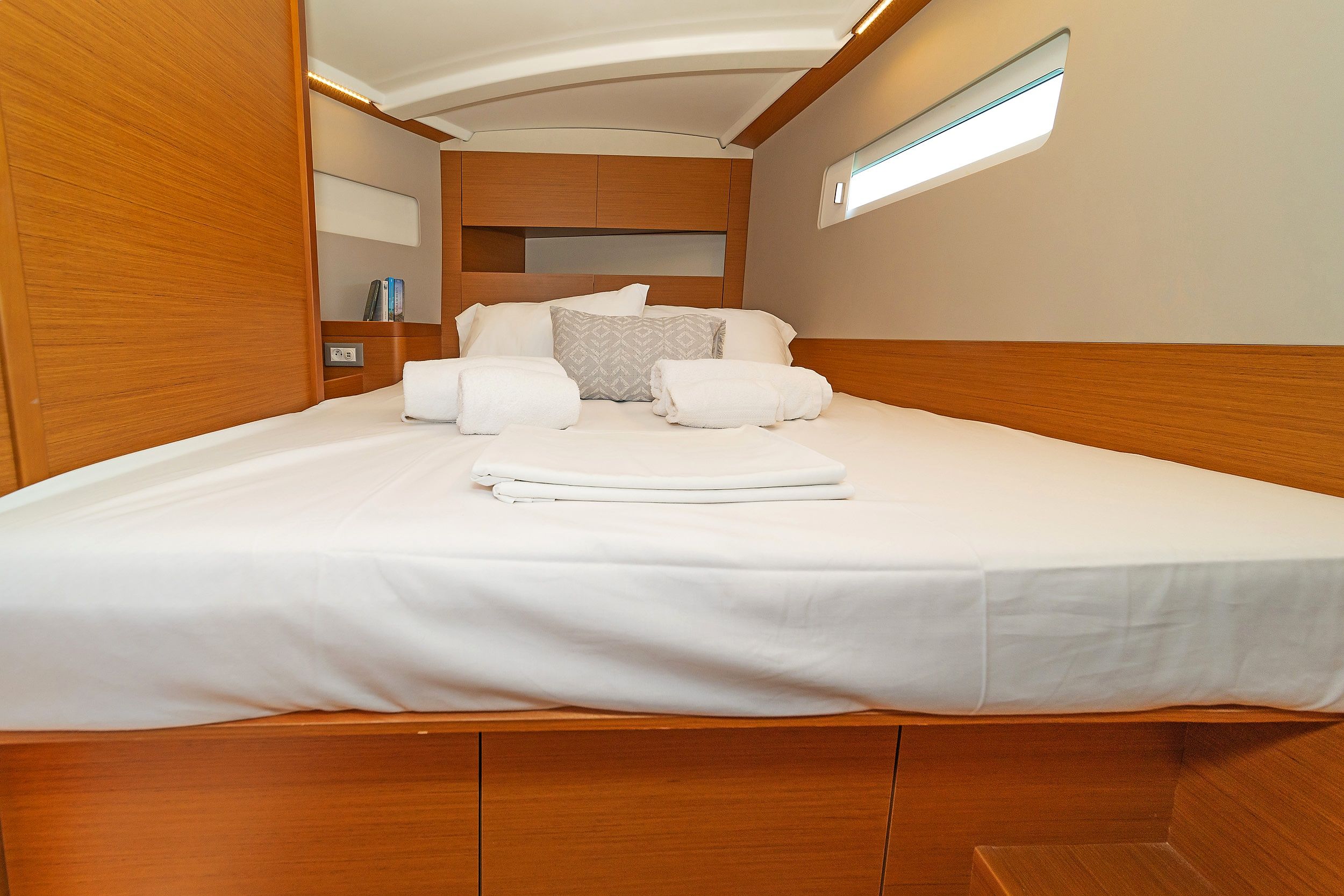 A neatly made bed with white linens and a round pillow in a cabin with wooden walls and a small window.