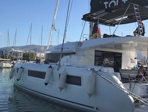 A white yacht docked at a marina with multiple masts, a covered area with seating, and a view of the marina and hills in the background. - Sun-Kissed Sailing Adventure in Islas Sarónicas (Alimos)