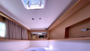 Quarto compacto e moderno com cama, janela com cortinas, claraboia e pequena área de cozinha.