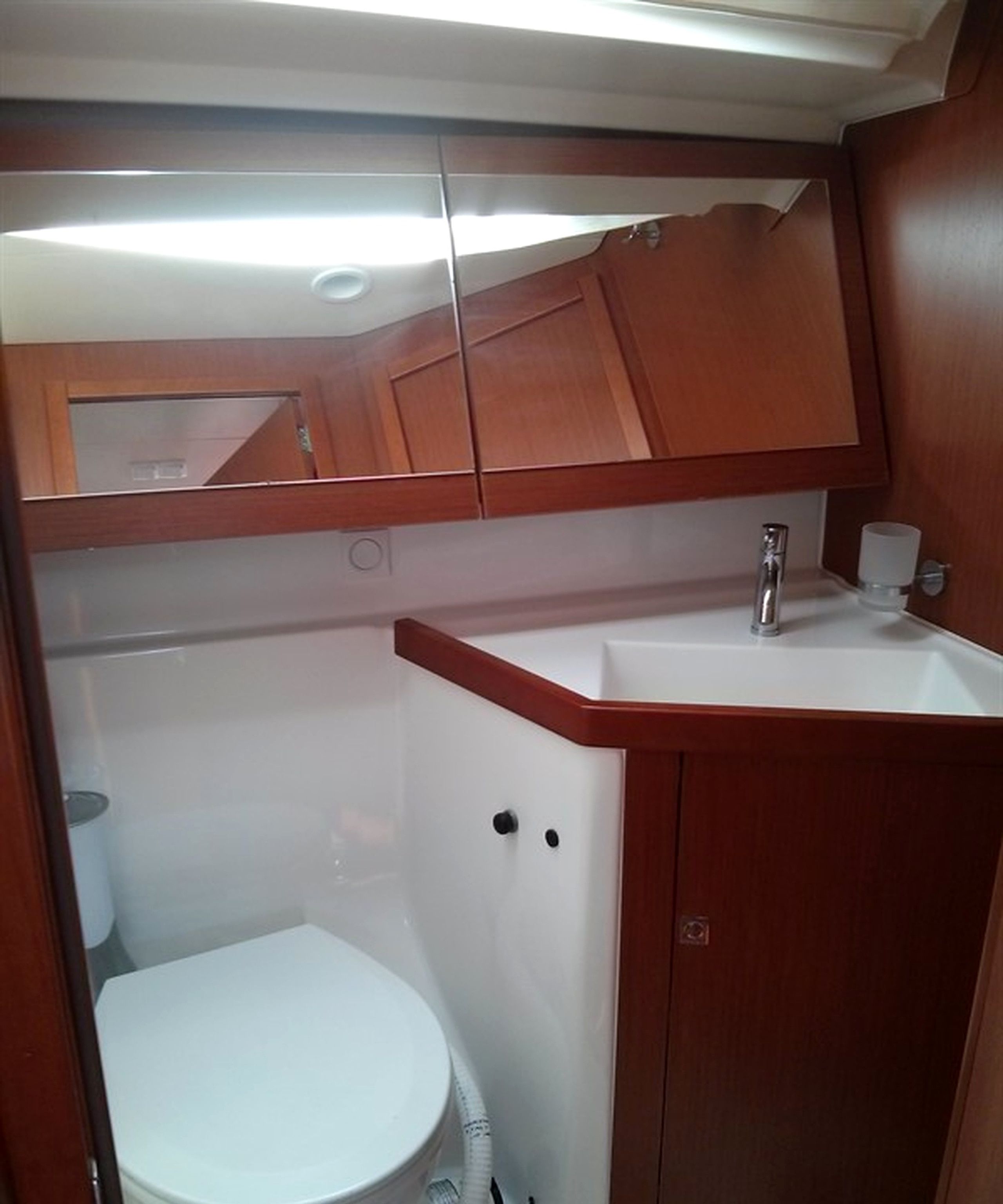 A compact bathroom with a white toilet, a sink, and a mirror above the mirror cabinet.