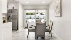 A modern kitchen with a stainless steel refrigerator, a dining area with a round table and four chairs, and a large window providing a view of the outdoors. - Modern home with Jacuzzi/ Near Siesta Key Beach (Sarasota)