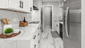 A modern kitchen with white cabinets, a stainless steel refrigerator, and a marble countertop. - Modern home with Jacuzzi/ Near Siesta Key Beach (Sarasota)