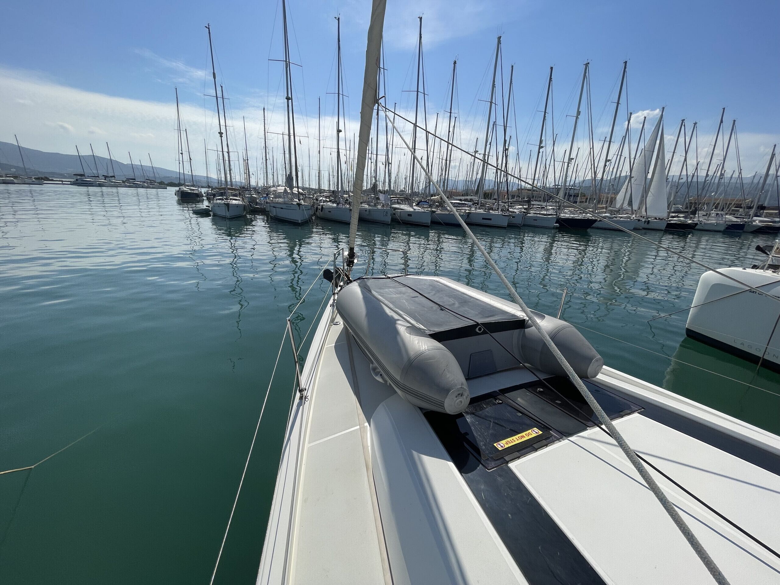 Un puerto deportivo con varios veleros amarrados, agua tranquila y cielo despejado.