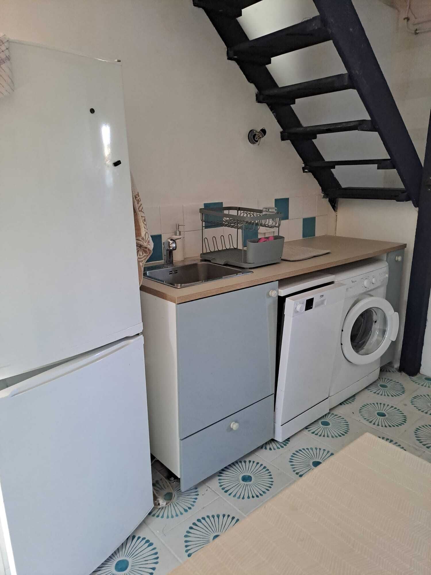 Une cuisine compacte équipée d’un réfrigérateur, d’un lave-linge et d’un évier avec un égouttoir.