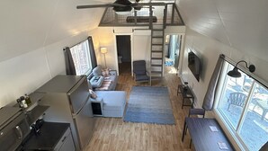 A compact kitchen with a dining area, a small living space, and a loft bedroom with a view. - Cozy Lofted Cabin #2 at Cataract Lake Getaway (Poland)