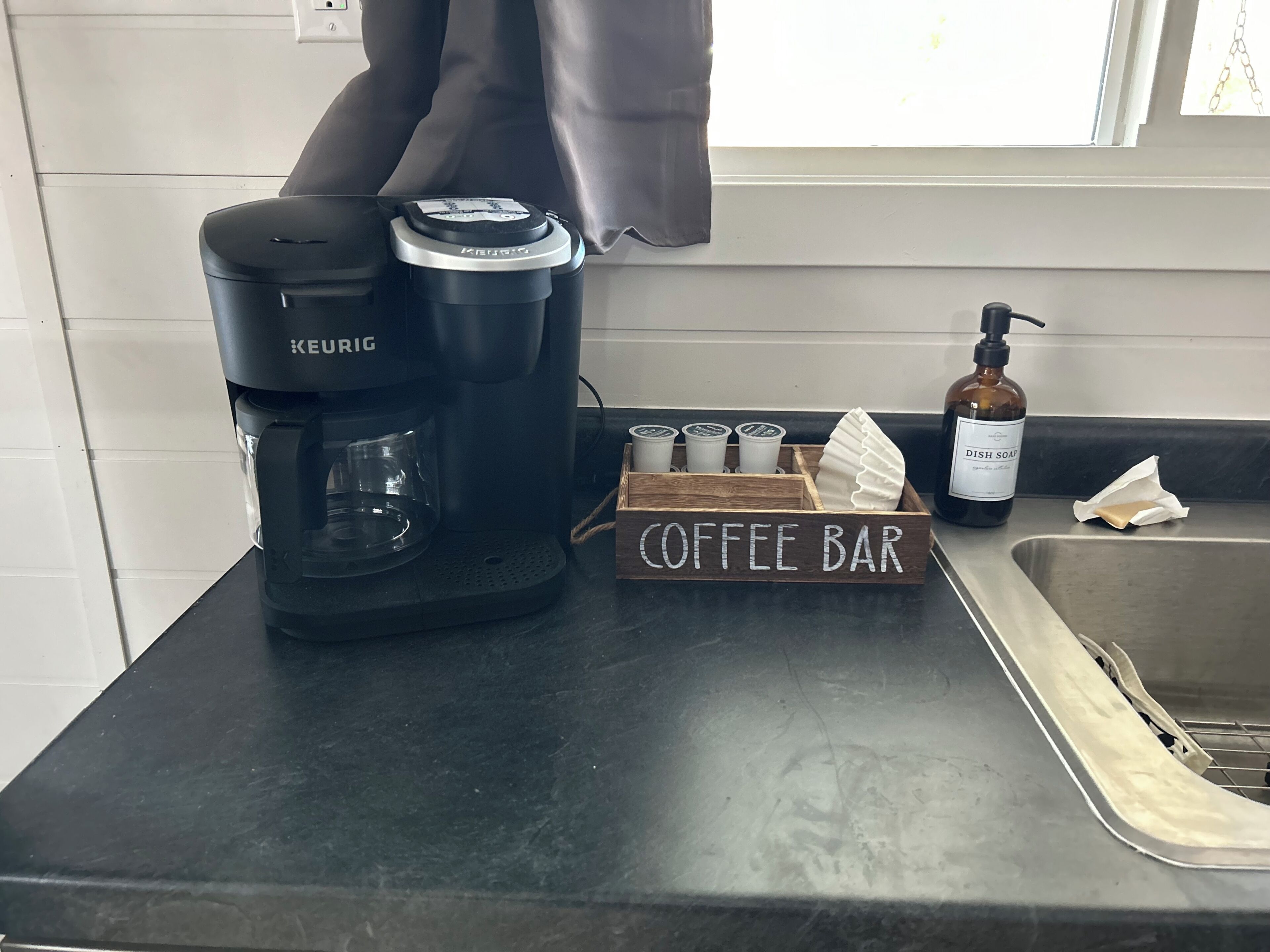 Keittiön työtasolla on Keurig-kahvinkeitin, kahvibaarin kyltti, astianpesuaineen pullo ja paperipyyheannostelija.