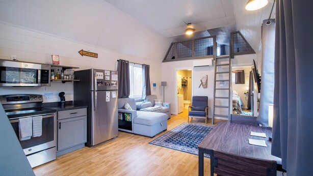 A compact kitchen with modern appliances, a dining area with a wooden table, and a cozy seating area with a sofa. - Cozy Lofted Cabin #2 at Cataract Lake Getaway (Poland)