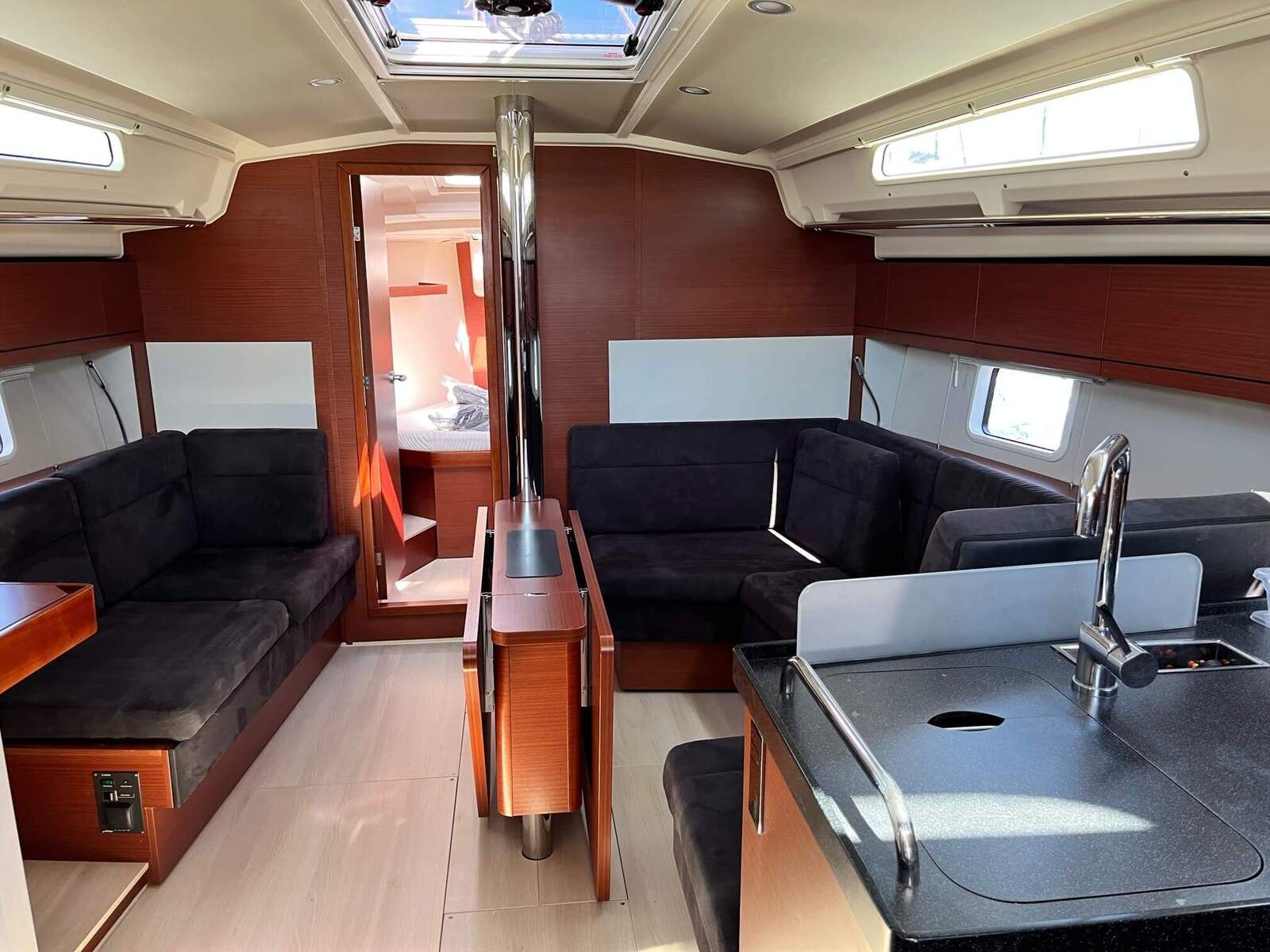 A compact interior with a central table, two sofas, a small kitchenette, and a skylight.