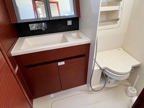 Een compacte badkamer met een witte wastafel, houten kastjes, een toilet en een spiegel boven de wastafel.
