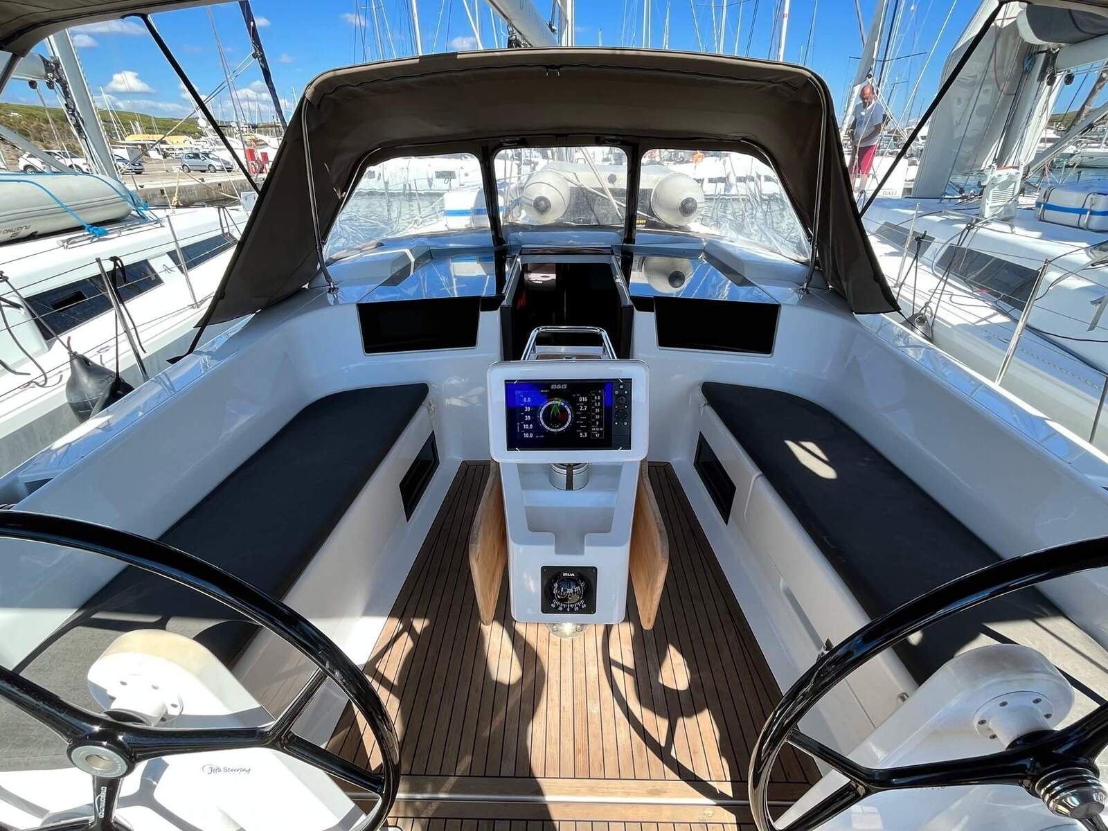 Interior de barco com console central, volante e vista do porto de iates.