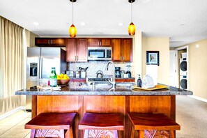 A modern kitchen with wooden cabinets, stainless steel appliances, a central island with bar stools, and pendant lighting. - Honua Kai 3 Free Cars KBM Resorts Front Alii Suite 3 Units, 6 Bedrooms HK Ml-3143 (Kaanapali)