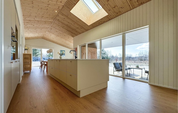 A spacious kitchen with a large island, wooden ceiling, and a view of the outdoors through large windows. - Gorgeous home in Sæby with WiFi (Sæby)