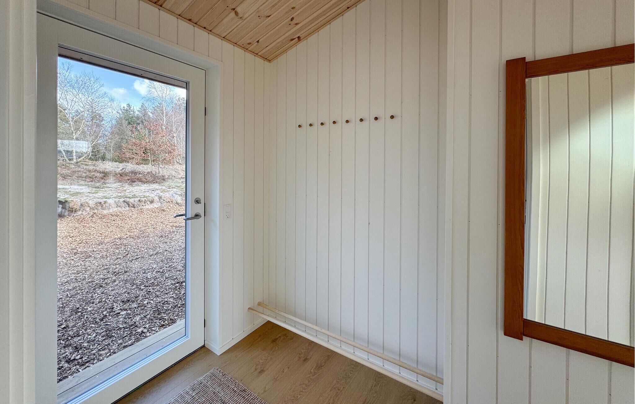 A room with a sliding glass door leading to an outdoor area, white paneled walls, a wooden ceiling, and a small rug on the floor.