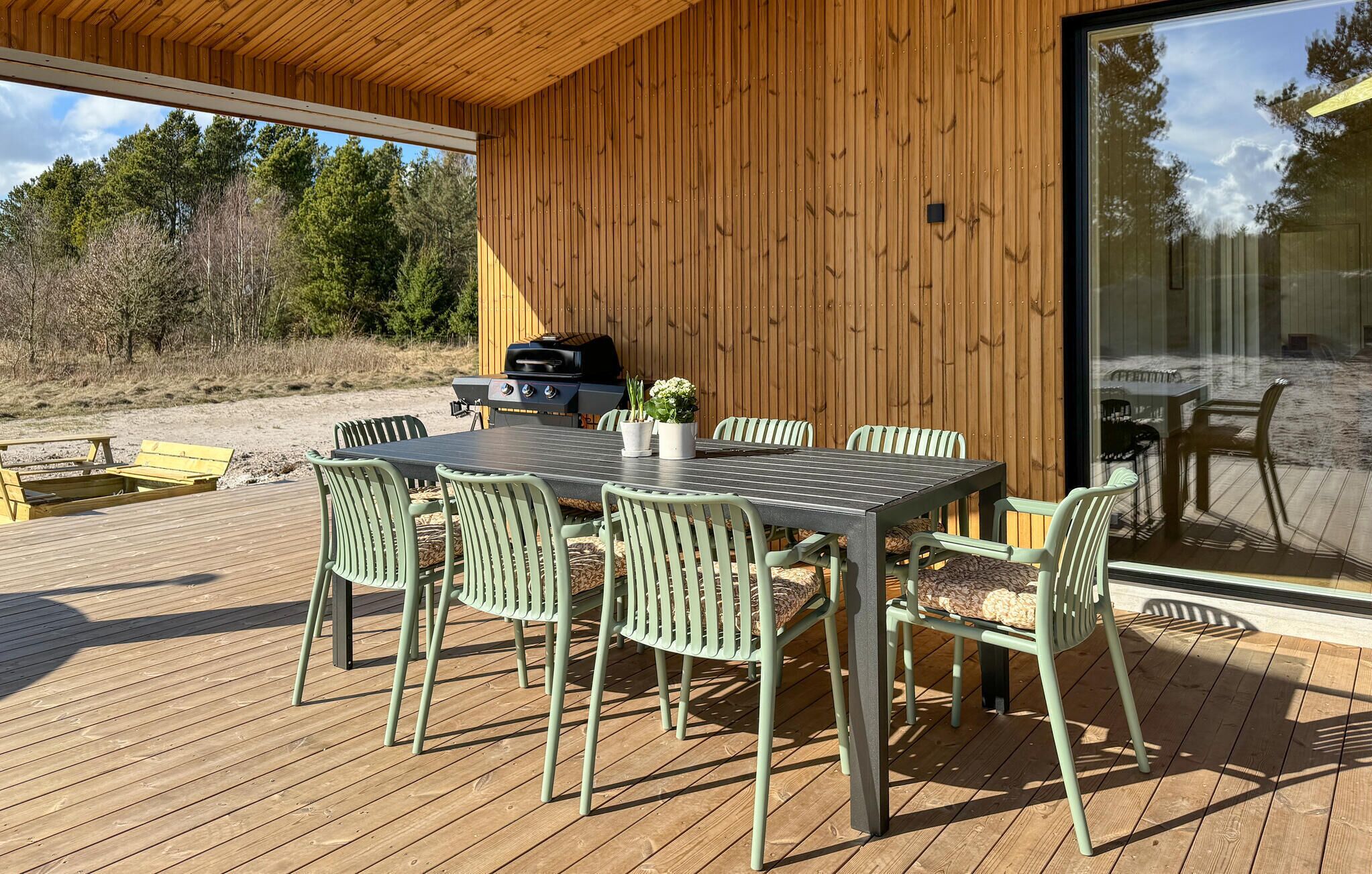 An outdoor dining area with a table and chairs, a grill, and a view of the surrounding landscape.