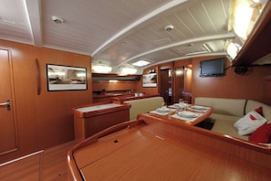A yacht interior with a dining area, a sofa, a television, and a kitchen. - Sun-Kissed Sailing Adventure in Islas Sarónicas (Alimos)