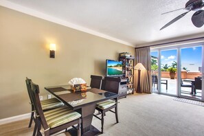 Ein Hotelzimmer mit Glastisch, gestreiften Stühlen, einem Fernseher, einem Bücherregal und Blick ins Freie.