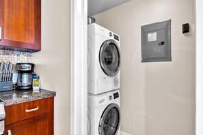 A compact laundry room with a stacked washer and dryer, a coffee maker, and a small cabinet with utensils. - Honua Kai 3 Free Cars KBM Resorts Front Alii Suite 3 Units, 6 Bedrooms HK Ml-3293 (Kaanapali)