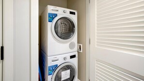 A stacked washer and dryer unit in a laundry room with a door and blinds. - Honua Kai 4 Free Cars KBM Resorts Front Alii Suite 4 Units, 8 Bedrooms HK Ml-3182 (Kaanapali)